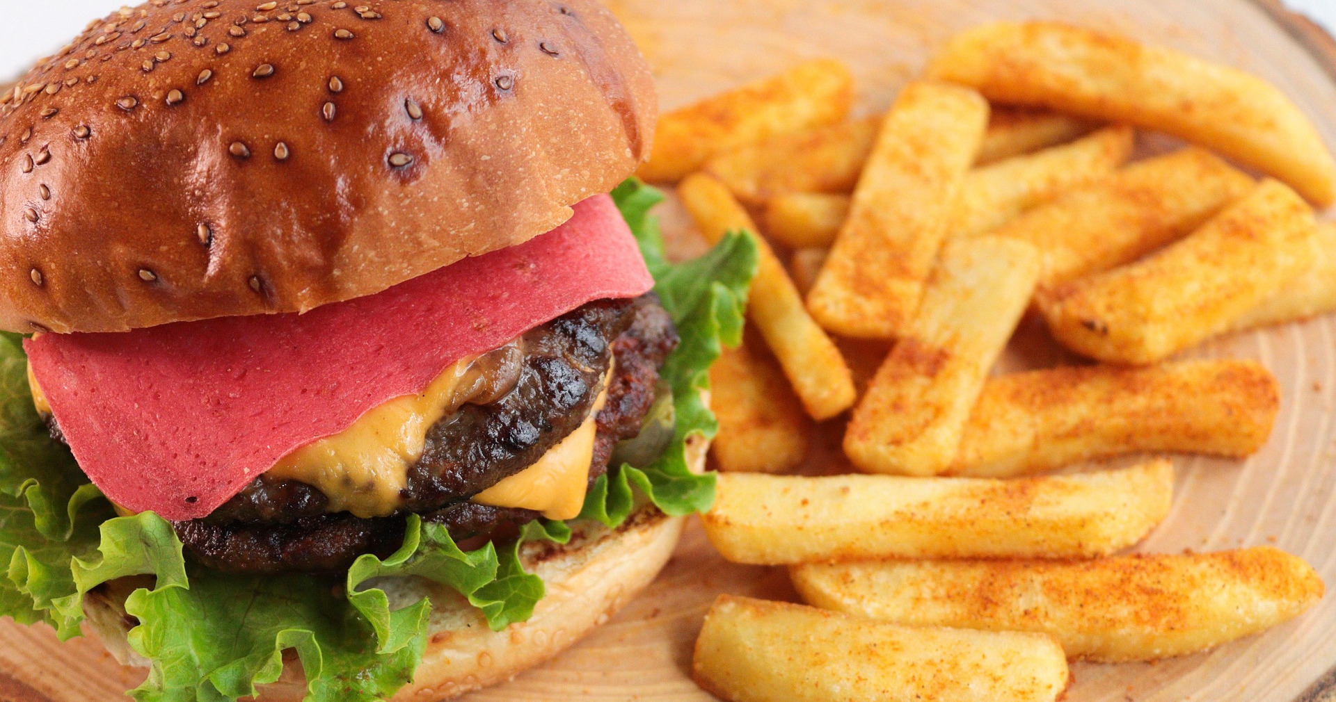 Saftiger Burger mit Salat, Tomate und Käse im Brötchen, serviert mit knusprigen Pommes frites.